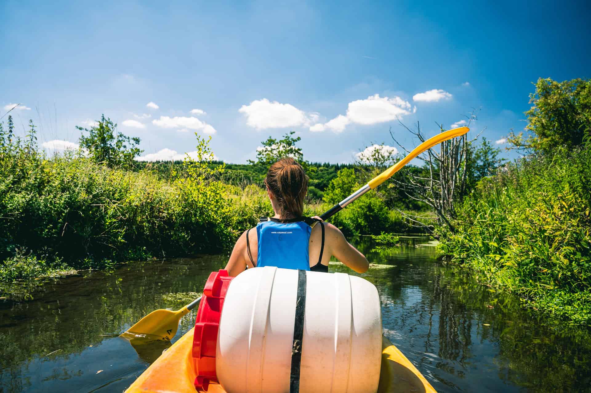 Cette photo montre un couple paddle-boarding sur un canal. Ils manient des paddles et semblent se déplacer tranquillement dans une environnement naturel. Le paysage est calme et l'eau est calade, ce qui permet de voir clairement les plants alentours et le ciel dégagé au-dessus. Cela donne à la photo un air de repos et de détente, qui pourrait attirer des personnes intéressées par l'activité de paddle-boarding ou cherchant du plaisir naturel. Le couple est en train d'apprécier leur environnement, ce qui suggère une expérience agréable et paisible.